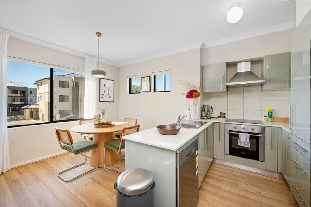 Modern kitchen and dining area with green cabinetry, a white island, and large sunlit windows.