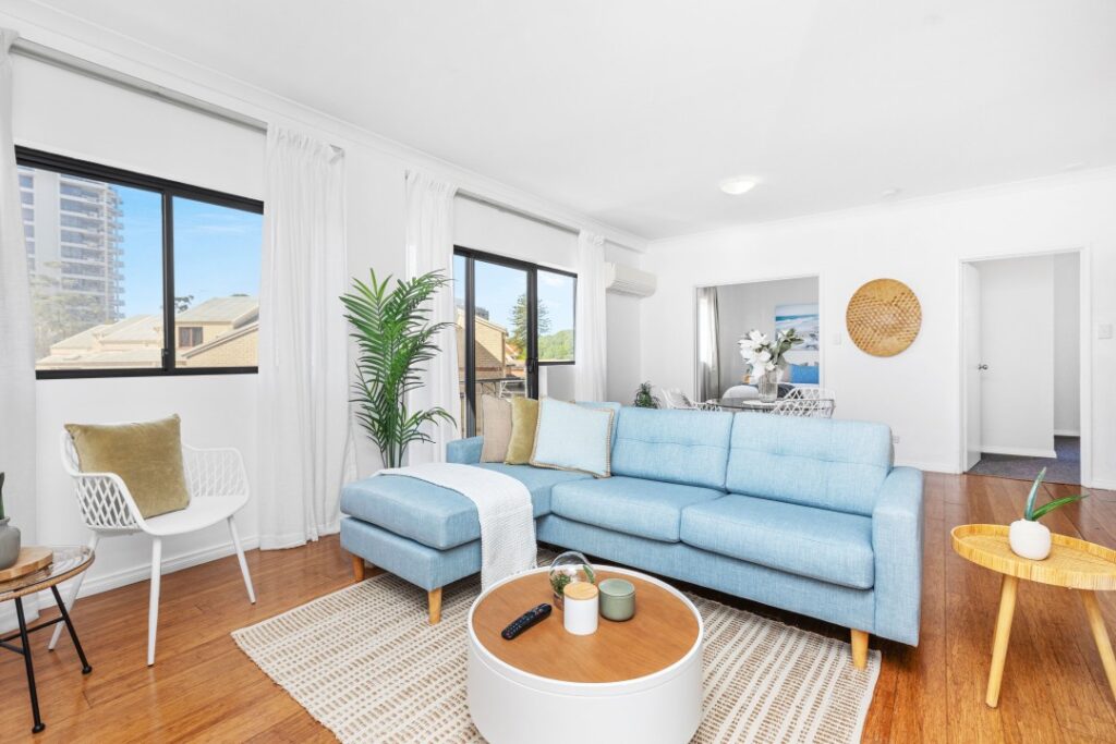 Bright living room with a blue sofa, white curtains, wooden floors, and coastal decor.