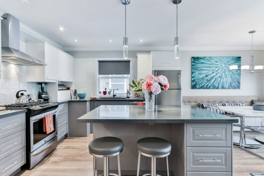 Modern grey kitchen with marble-look countertop, warm under-cabinet lighting, coffee machine, ceramic soap bottles, chopping board with fresh produce, and stainless steel oven with digital display