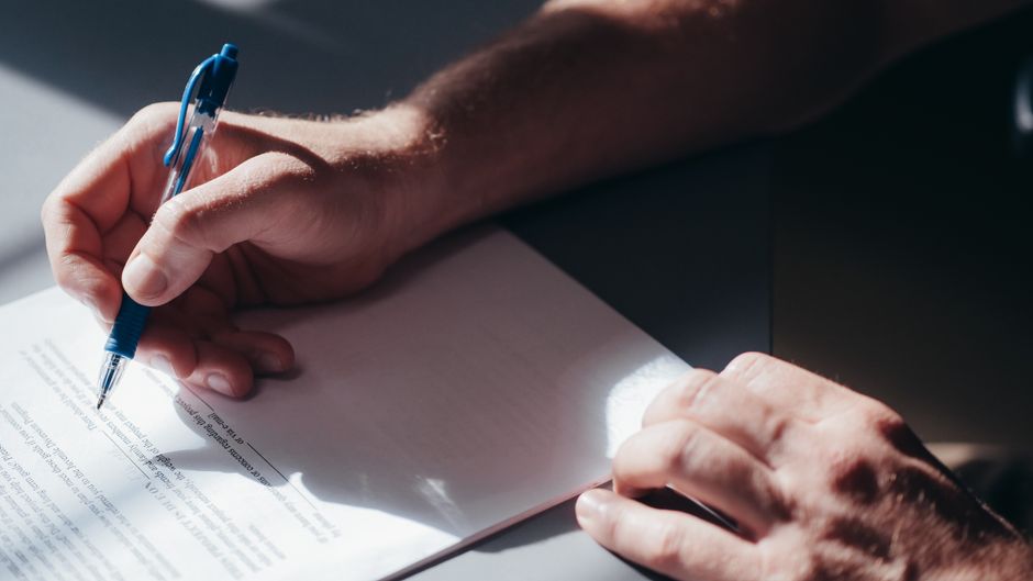 Hand signing document with blue pen, representing STRA registration and compliance.