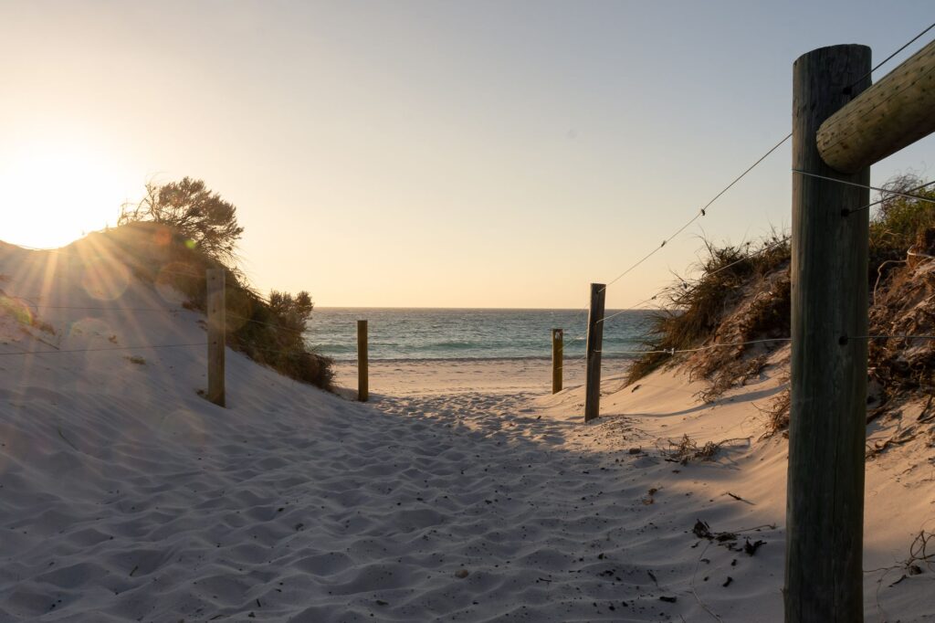 Sandy pathway with wooden posts leading to beach at sunset, Western Australia.