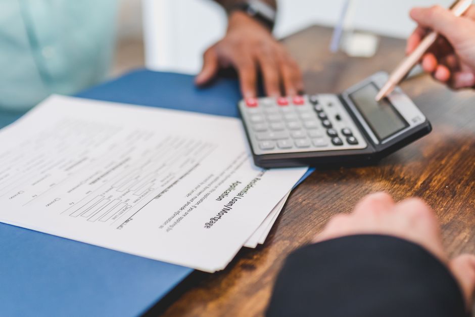 Hands using calculator with real estate documents on desk for financial review.