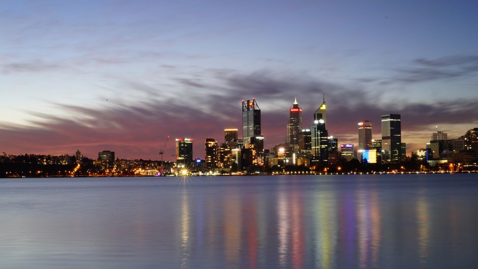 Perth city skyline illuminated at dusk, reflecting across the Swan River.