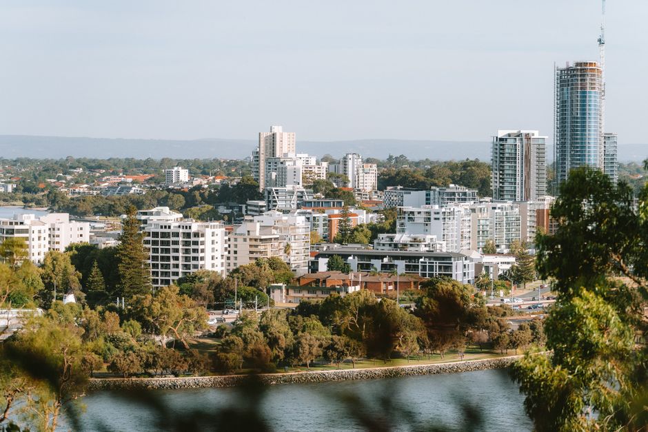 Perth skyline and Swan River surrounded by trees and green vegetation.