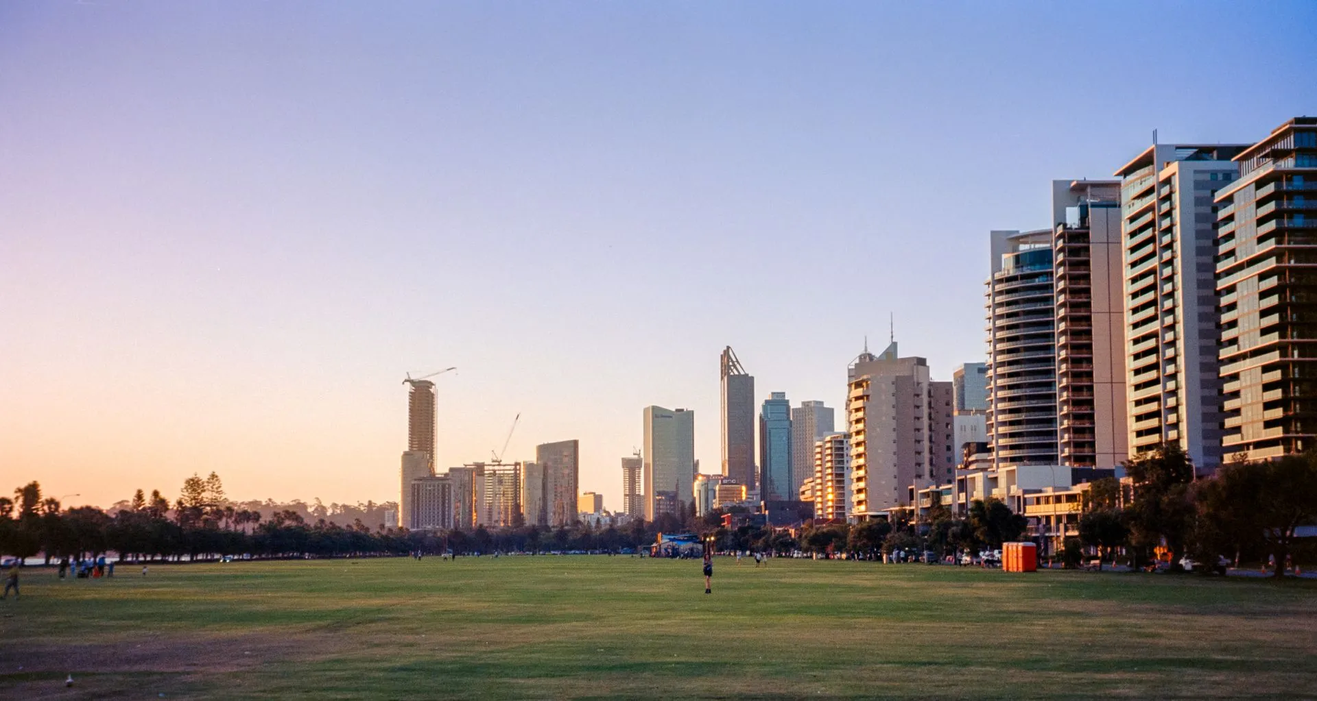 Perth city skyline at sunset seen across a grassy park